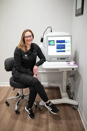 A smiling woman sitting on a chair in front of a table with a monitor and a medical device