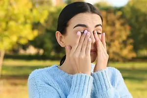 A woman with her eyes closed and hands covering her face in a park