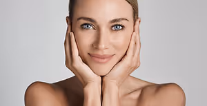 A woman with a smiling face is posing for the camera with both hands on her cheeks