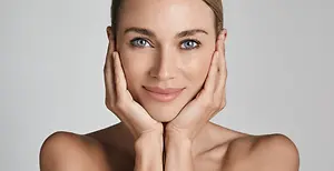 A woman with a smiling face is posing for the camera with both hands on her cheeks