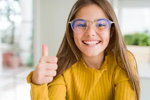 A girl with glasses smiling and giving a thumbs up in a room