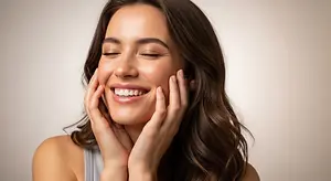 A woman is smiling with her eyes closed and her hands on her cheeks.