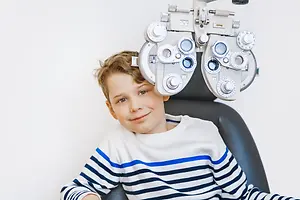 A young boy is smiling while sitting in front of an eye test machine.