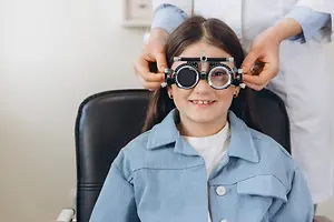 A girl is sitting in a chair while a doctor adjusts her eyeglass frame.