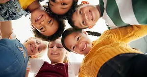 A group of happy children smiling and standing in a circle, likely in a classroom or school setting.