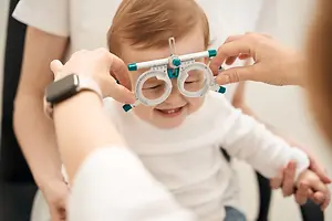 A baby is smiling while a doctor adjusts his eyeglass frame in a clinic.