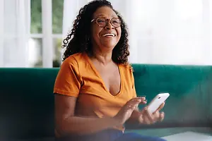 woman smiling and laughing while sitting on a couch and using her phone