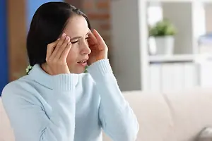 A woman sitting on a couch with her hands on her forehead, she seems to be crying.