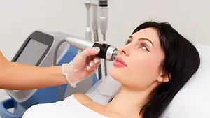 A woman lying on a bed getting her face treated with a laser device.