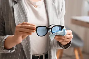 A woman is cleaning her glasses with a blue cloth.