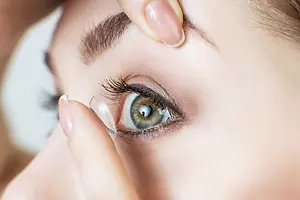 A woman is putting in a contact lens on her eye.