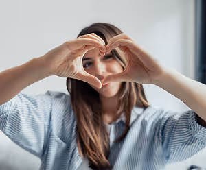 Woman forming a heart shape with her hands in a living room