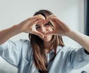Woman forming a heart shape with her hands in a living room