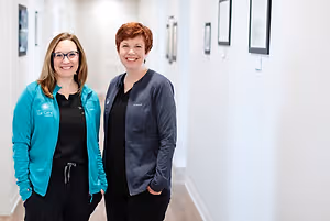 Two women stand in a hallway and smile for a photograph