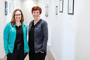 Two women stand in a hallway and smile for a photograph