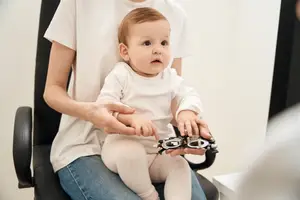 A woman holding a baby who is examining an ophthalmoscope