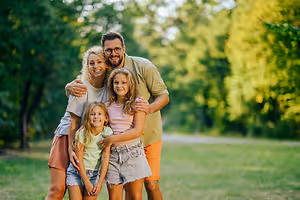 A family of four standing in a park with green grass and trees in the background