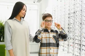 A woman and a young boy are standing in front of a wall with eyeglasses displayed.
