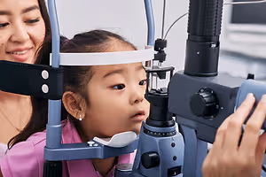 A young girl is having her eyes examined by a doctor with a black and blue machine.