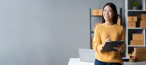Asian businesswoman standing in office with clipboard, smiling at camera