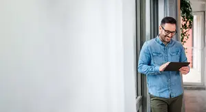 Man in a denim shirt holding a tablet and smiling