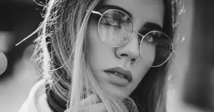 A black-and-white photo of a woman wearing glasses and a white hoodie with a ring on her nose