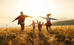 A family of four is enjoying a day outdoors in a grassy field with mountains in the background, under a setting sun.