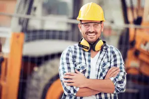 A man with glasses and a yellow hard hat smiling at the camera at a construction site