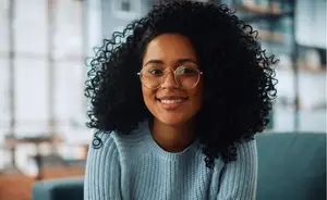 Image of a woman wearing a blue sweater and glasses with curly hair and smiling
