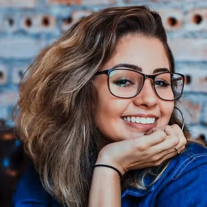A woman with glasses and a denim jacket smiling at the camera.