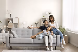 A family of three, a woman, a man, and a young girl, sitting on a couch and smiling while posing for a photo