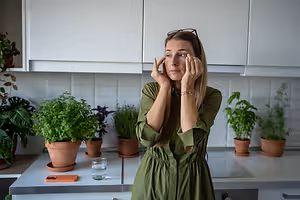A woman standing in a kitchen holding her face with both hands