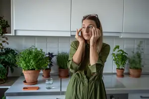 A woman standing in a kitchen holding her face with both hands