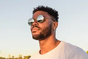 A man wearing sunglasses and a white t-shirt is looking to the right.