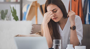 Woman sitting at a desk with her hands covering her face, looking stressed or in pain