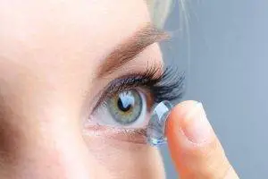 A woman putting a clear contact lens in her eye.