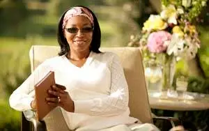 Woman in white shirt and sunglasses sitting on a chair holding a brown notebook