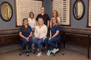 Seven people in blue uniforms sitting in front of a wall with glasses on it.