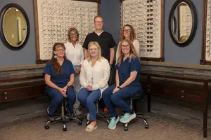 Seven people in blue uniforms sitting in front of a wall with glasses on it.