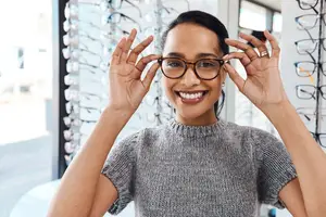 woman smiling while trying on a pair of glasses