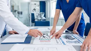 Three optometrists working on an eye exam chart on a desk.