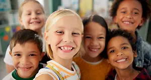 A group of children are smiling and posing for a selfie in a classroom.