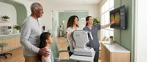 A group of people in a doctor's office. One of them is pointing at a monitor with a green image on it. The people are smiling and looking at the monitor.