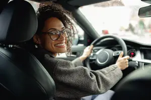 Woman wearing glasses driving a car and smiling