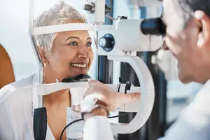 An elderly woman is having her eyes examined by a male doctor in a white coat.