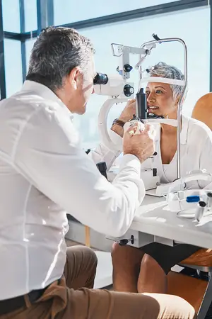 A man doctor is examining a woman's eye with an eye exam machine in an office