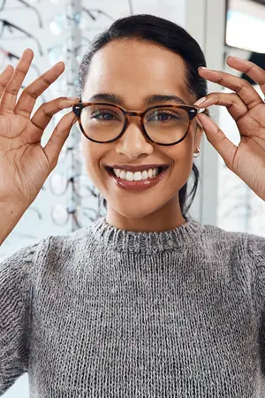 A woman wearing glasses is smiling and holding her glasses in her hands.