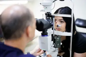 A man is using an ophthalmoscope to examine a woman's eye in a clinic.