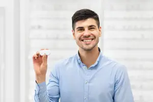 A man holding two contact lenses and smiling at the camera