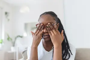A woman with glasses covering her eyes with her hands in a living room